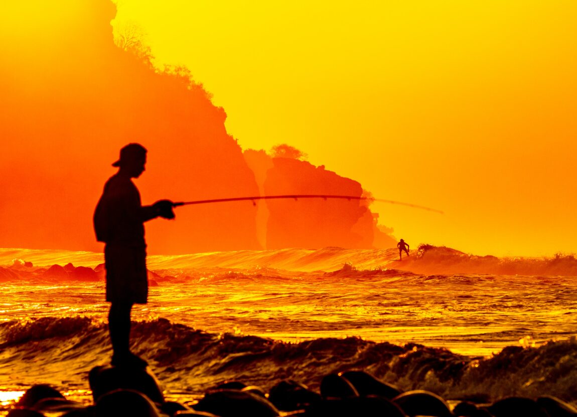 man fishing in sea during orange sunset